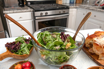 Freshly prepared Caesar salad in a glass bowl is on the kitchen table. Grilled chicken, crackers and ingredients.