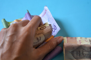 Hand putting Indonesian rupiah money into traditional Indonesian white piggy bank, on white  background. close up. view top