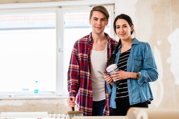Portrait of a happy young couple wearing casual clothes while holding tools for home remodeling...