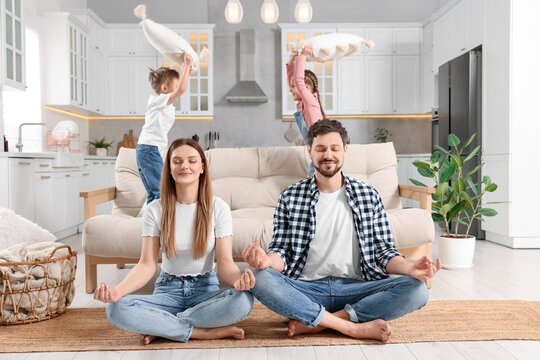 Parents meditating while their children playing with cushions at home