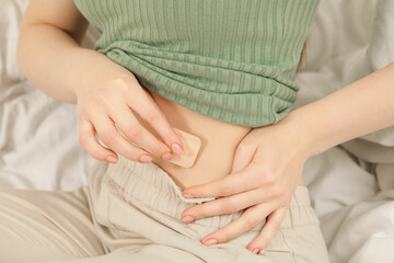 Woman applying contraceptive patch onto her belly on bed, closeup