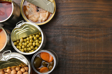 Open tin cans with different products on wooden table, flat lay. Space for text