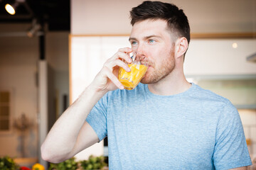 Fototapeta premium Handsome young man drinking orange juice in kitchen in the morning
