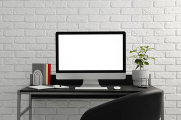 Stylish workplace with computer, houseplant and stationery on table near white brick wall