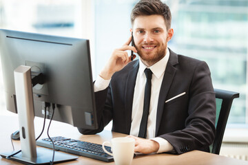 Young businessman at the office sitting at his desk and talking on a phone