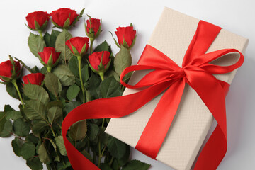 Beautiful gift box with bow and red roses on white background, top view