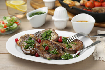 Tasty beef tongue pieces, salsa verde and berries on beige wooden table, closeup