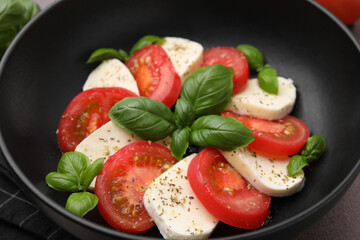 Caprese salad with tomatoes, mozzarella, basil and spices in bowl, closeup