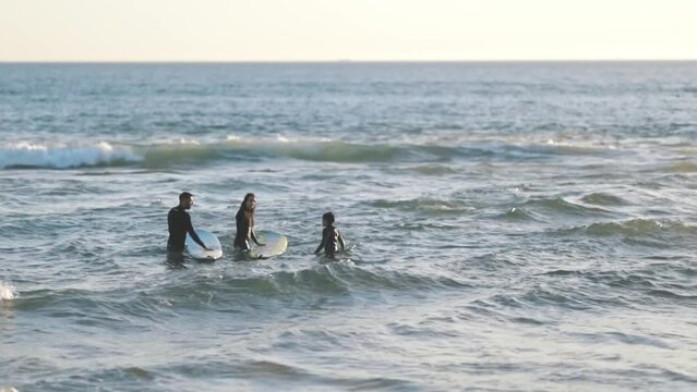 Family of surfers teaching their little son in sea
