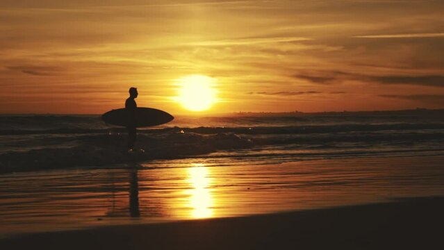 Silhouette of athletic surfer at sunset in waves