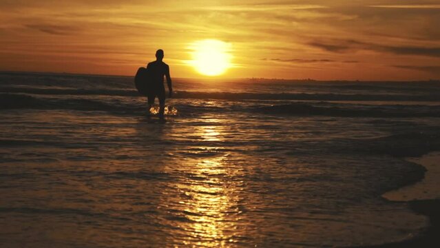 Silhouette of surfer at sunset in waves of sea