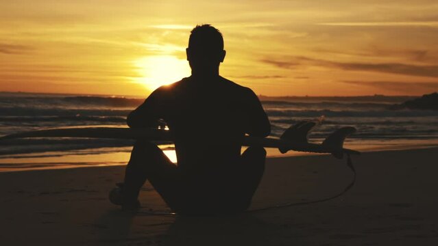 Silhouette of surfer sitting on beach at sunset