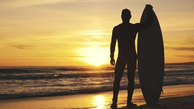 Silhouette of man at sunset with surfboard by sea