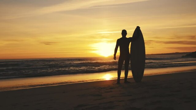 Silhouette of athletic surfer looking at sunset 