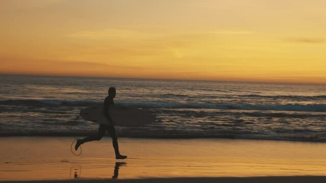 Silhouette of athletic surfer running on beach