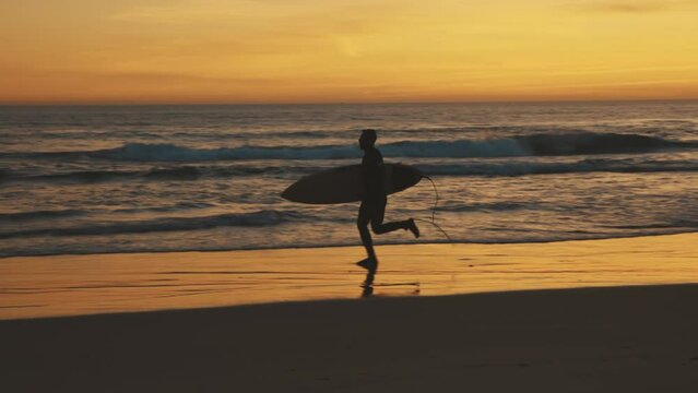 Surfer running by the ocean at sunset