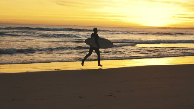Surfer with board running by ocean at sunset
