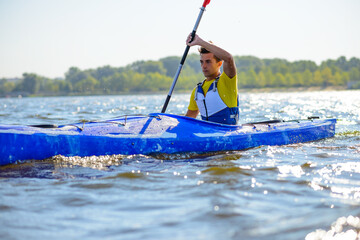 Naklejka premium Young Professional Kayaker Paddling Kayak on the River under Bright Morning Sun. Sport and Active Lifestyle Concept