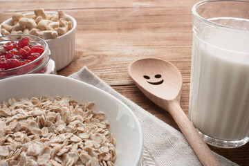 Oatmeal with dried cherries and cashews on wooden table whith napkin. Glass of milk. Wooden spoon.