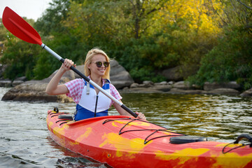 Young Woman Paddling Kayak on the Beautiful River or Lake among Stones at the Evening