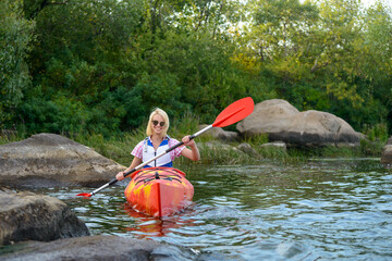 Young Woman Paddling Kayak on the Beautiful River or Lake among Stones at the Evening