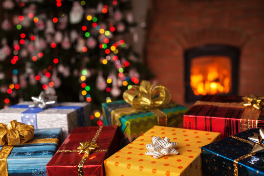 Many christmas presents in front of xmas tree and fireplace in a dark room