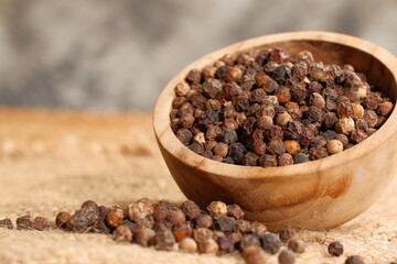 Closeup black pepper seeds or peppercorns (dried seeds of piper nigrum) in wooden bowl