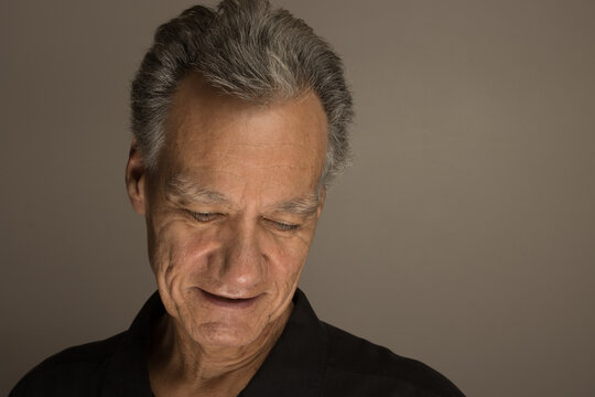 Portrait of a mature man with graying hair wearing a black shirt 60plus looking down