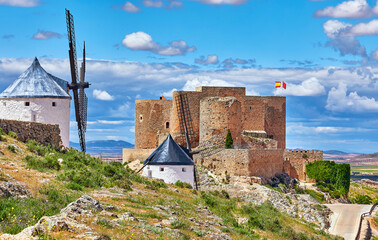 Wind mills and old castle in Consuegra, Toledo, Castilla La Mancha, Spain. Picturesque landscape with view to ancient walls and windmills on blue sky with clouds.