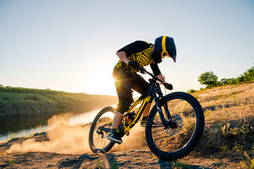 Fototapeta premium Professional Cyclist Riding the Downhill Mountain Bike on the Summer Rocky Trail at the Evening. Extreme Sport and Enduro Cycling Concept.