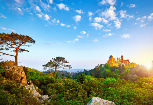 Sintra, Lisbon, Portugal. Palace of Pena in park among green trees, forest and stone rocks. Sun, morning sunrise on sky with clouds.