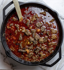 Homemade beef Chili in a rich savory sauce with onions, corn, beans, steak, and carrots in a cast iron pot