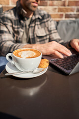Portrait of a handsome successful smart man drinking coffee and looking at a laptop. A business man is having breakfast sitting on a beautiful terrace in a cafe. Reading, browsing the Internet