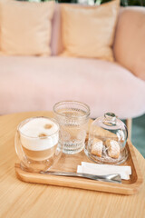 Cup of coffee cappuccino with cantuccini and a glass of water on a wooden tray. Coffee with milk, a cookie and a glass with water on a glass table.