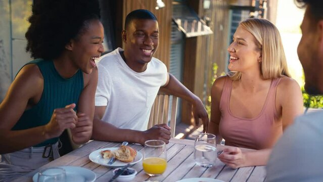 Smiling group of smiling friends on holiday eating breakfast outdoors together looking at mobile phone  - shot in slow motion