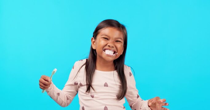 Smile, toothpaste and toothbrush for child in studio, morning routine for clean mouth and happiness. Brushing teeth, wellness and face of happy girl on blue background, cleaning and care for children
