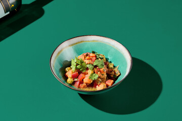 Side view of salmon tartare with mango-chili sauce, served in a ceramic bowl in an Asian restaurant. Green backdrop. Stark shadows. Minimalistic and contemporary