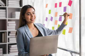 Businesswoman working on laptop and writing strategy ideas of new business project in sticky notes