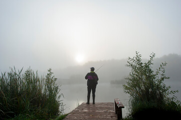 a fisherman on the shore of a pond pulls a spinning fish on a cloudy day