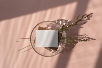 Blank paper card mock up, envelope, meadow grass, glass vase with aesthetic abstract sunlight shadow on pastel pink background, elegant wedding invitation, greeting card, business brand template