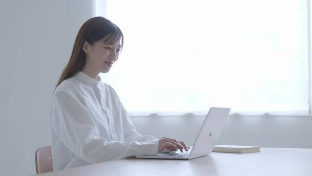 リビングにてノートパソコンを使用してリモートワークを行う30代の日本人女性