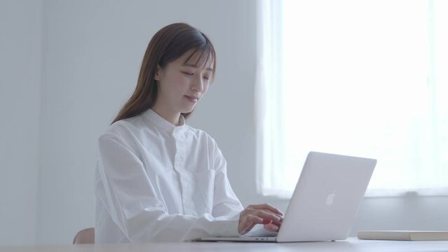 リビングにてノートパソコンを使用してリモートワークを行う30代の日本人女性