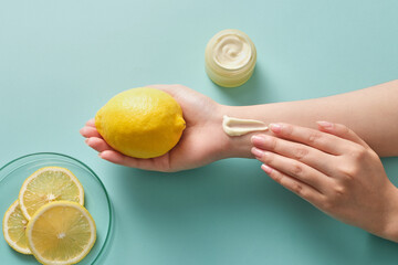 On a blue background, a fresh lemon on palm and the other hand applying cream texture. Mockup scene...