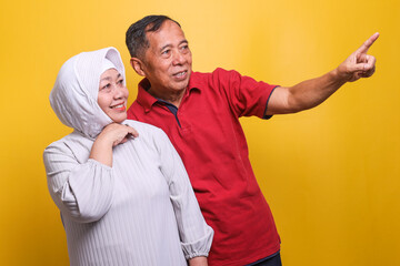 Smiling elderly Asian couple looking and pointing at copy space on yellow background. 