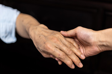 close up of a wrinkled hand is holding a young hand. 