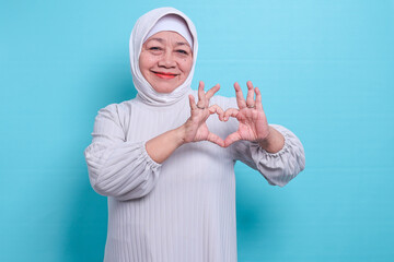 Smiling happy elderly Asian woman wearing  hijab showing love, making heart shape fingers
