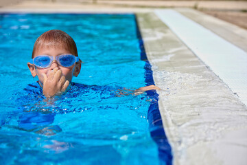 Happy boy diver learns to swim in the pool. Water activities of the child in the summer in the pool with clear blue water