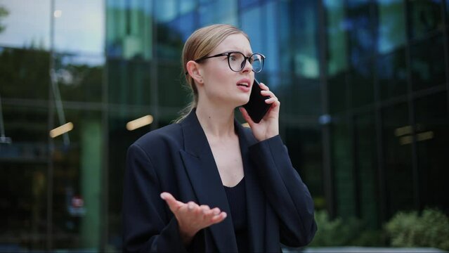 Frustrated assertive young business woman having heated conversation on her mobile phone outdoor. Unsatisfied female customer expressing dissatisfaction frustration, using strong language and arguing.