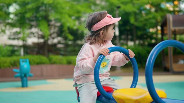 Little girl holds handle while bouncing up and down on playground seesaw.