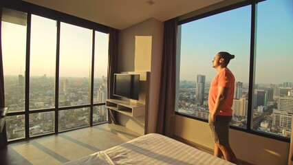 Handsome man in his room in luxury hotel is looking beautiful sunrise. Nice guy lives or...